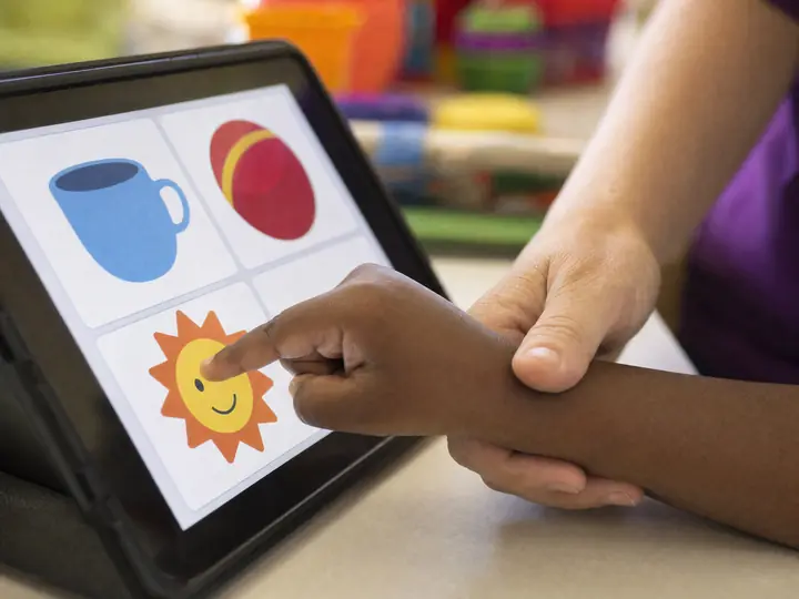 O dedo de uma criança tocando uma figura numa prancha de comunicação no tablet